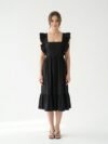 Mannequin portant la robe mi-longue noire 'Shadow' avec encolure carrée, bretelles à volants et jupe froncée, de la marque Divine Dress.