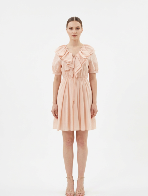 Mannequin portant la robe courte couleur pêche 'Peach' avec large col à volants, lien à nouer et manches courtes bouffantes, de la marque Divine Dress.