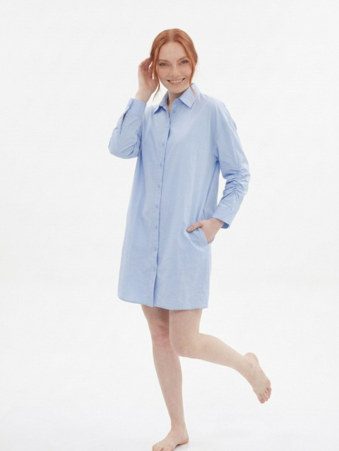 Mannequin souriante portant la robe chemise courte bleu pâle 'Aura' avec manches longues froncées et coupe ample, de la marque Divine Dress.