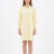 Mannequin souriante portant la robe chemise courte jaune pâle 'Aura' avec manches longues froncées et coupe ample, de la marque Divine Dress.