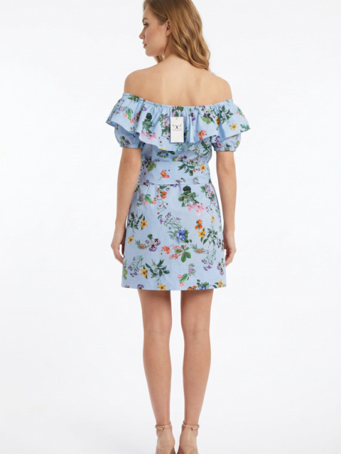Mannequin portant la robe courte bleu clair à imprimé floral 'Bow Elegance', avec encolure Bardot à volants et grande ceinture nouée, de la marque Divine Dress