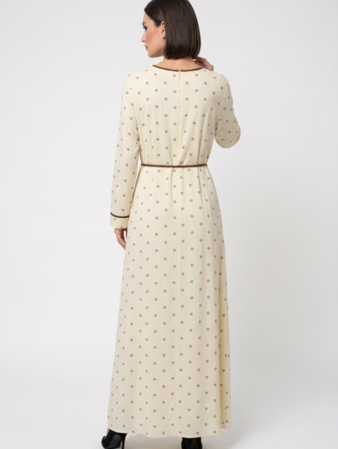 Mannequin portant la robe longue crème à petits motifs 'Clarity', avec manches longues, fleur décorative au col et fine ceinture à nouer marron, de la marque Divine Dress.