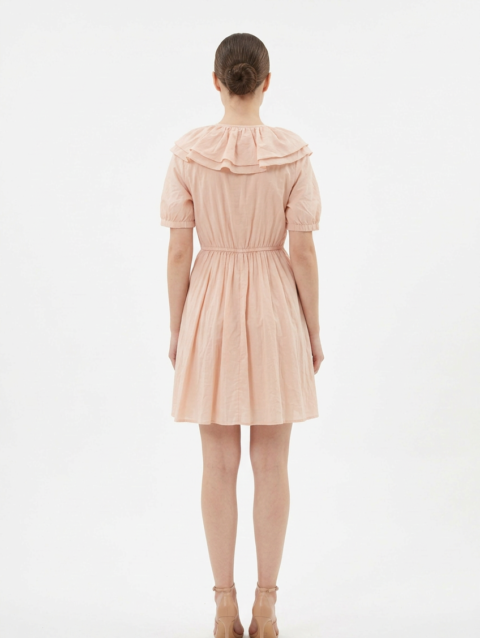 Mannequin portant la robe courte couleur pêche 'Peach' avec large col à volants, lien à nouer et manches courtes bouffantes, de la marque Divine Dress.