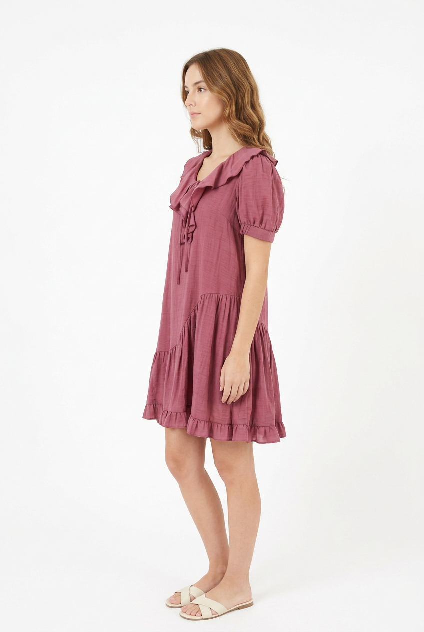 Mannequin portant la robe courte vieux rose 'Cascading' avec col à volants, manches courtes bouffantes et jupe asymétrique, de la marque Divine Dress.
