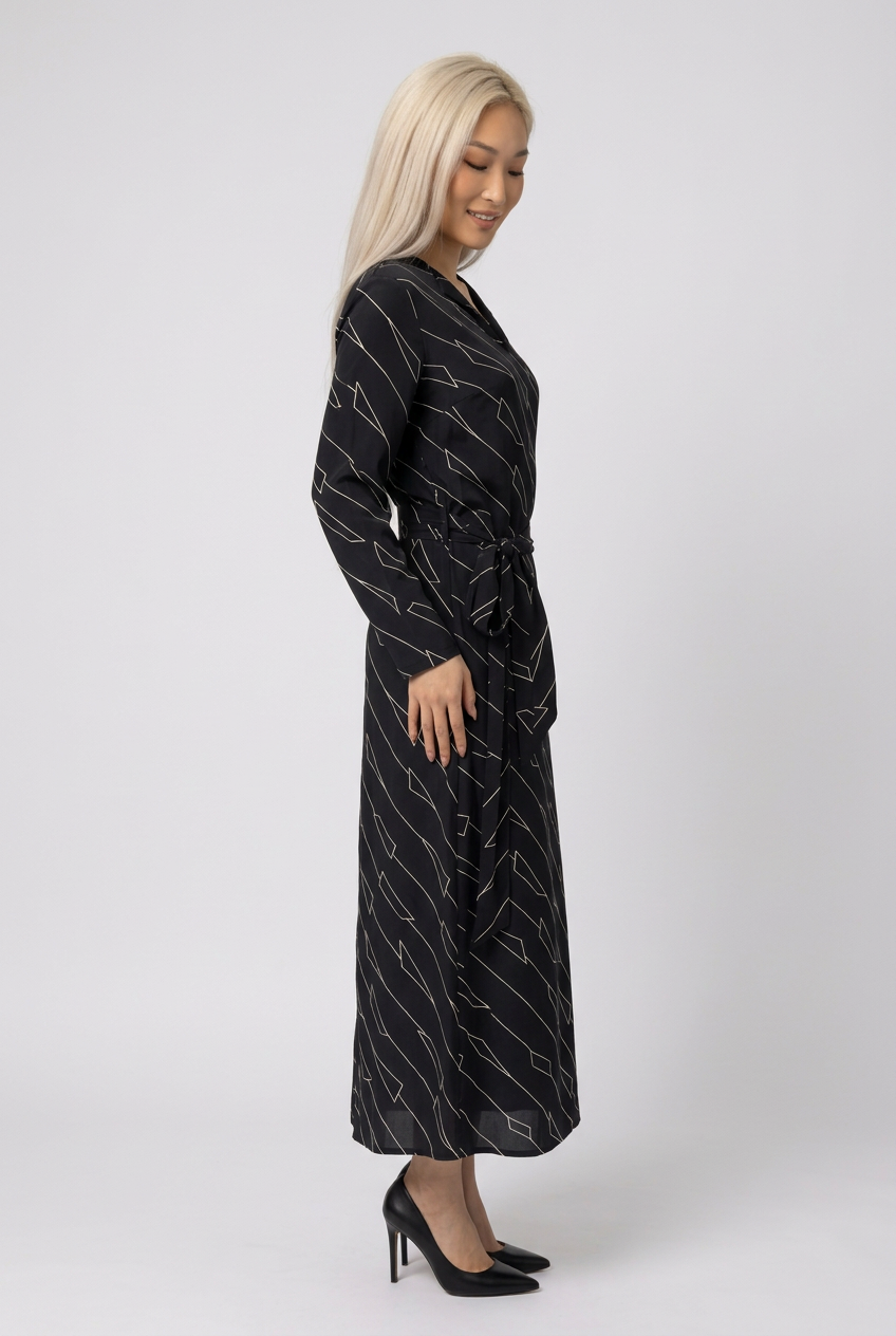 Mannequin portant la robe longue noir à motif géométrique 'Geometric Grace', avec col en V, manches longues et ceinture à nouer, de la marque Divine Dress.