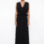 Mannequin portant la robe longue fluide noir 'Athena' avec décolleté en V, taille froncée à cordon et détails volantés, de la marque Divine Dress.