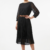 Mannequin portant la robe midi noir 'Velvet Touch' avec jupe plissée, manches 3/4 et large ceinture décorative, signée Divine Dress.