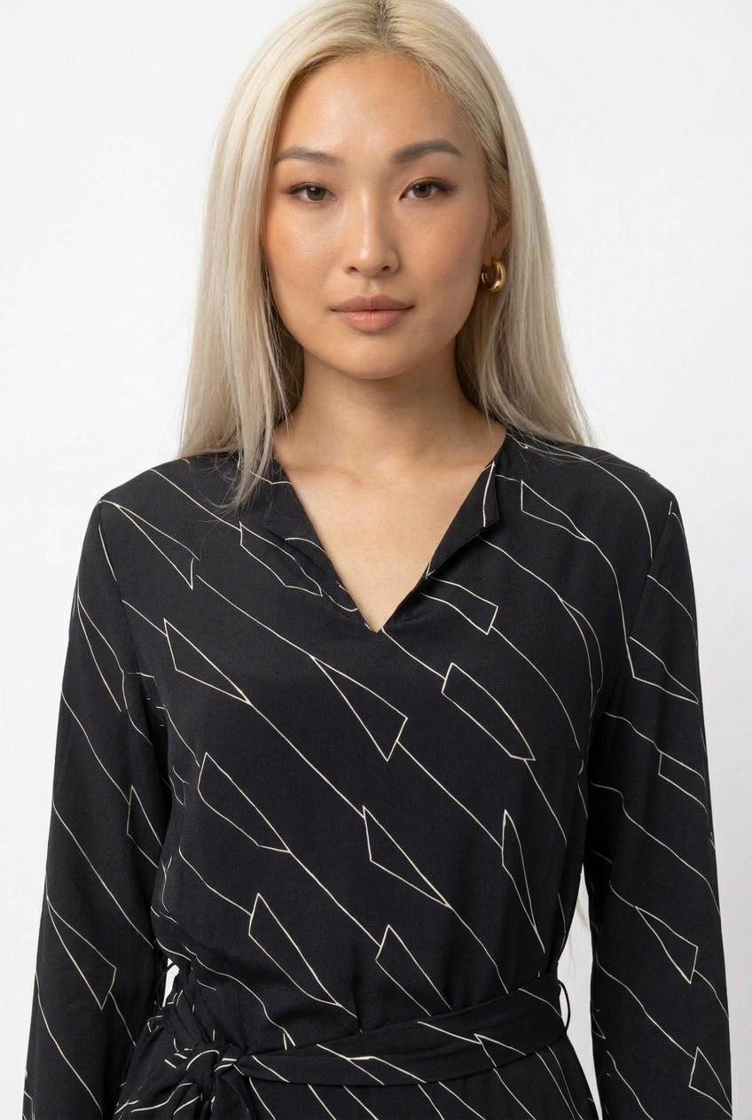 Mannequin portant la robe longue noir à motif géométrique 'Geometric Grace', avec col en V, manches longues et ceinture à nouer, de la marque Divine Dress.